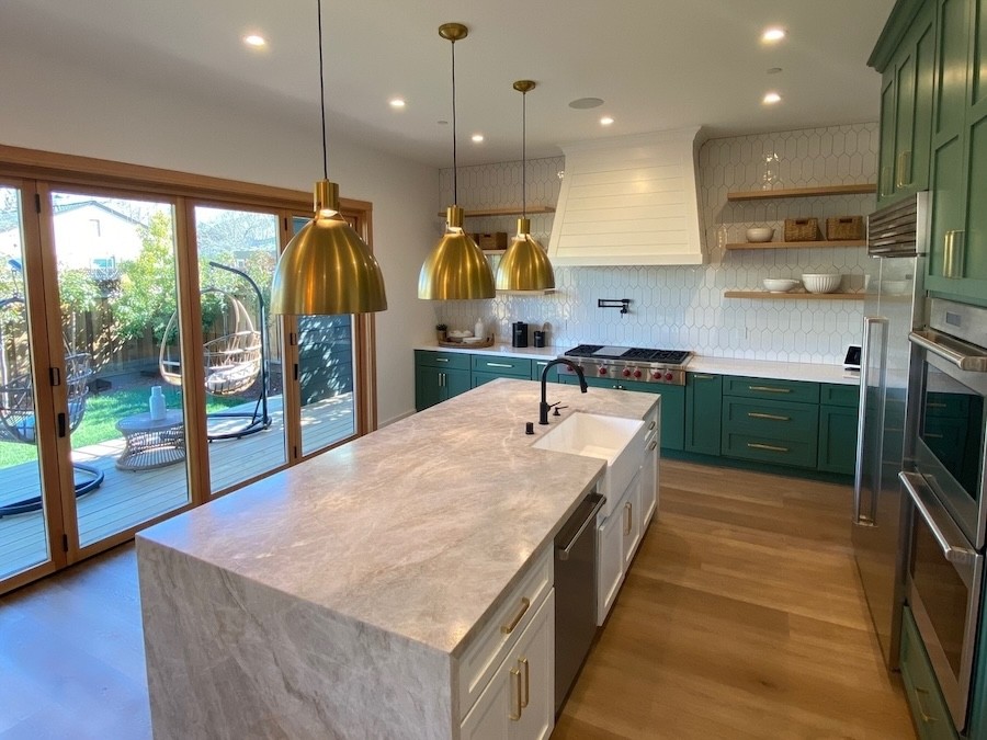 gold pendant lights above a white stone countertop. Recessed lights in the ceiling illuminate the kitchen.