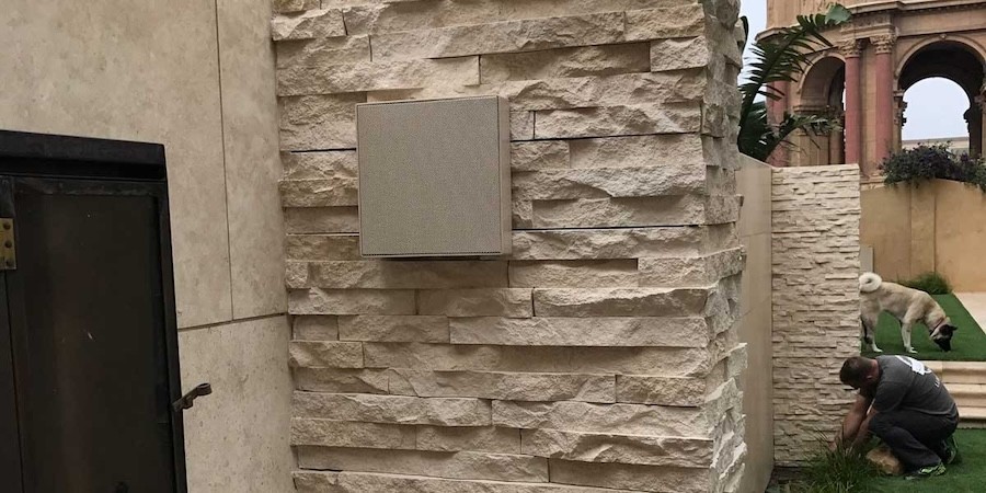 A speaker installed flush against a faux brick wall in a backyard.