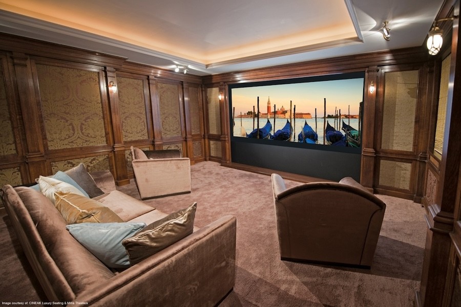 Luxurious home theater with plush seating, wood paneling, and a large screen displaying a waterfront view.